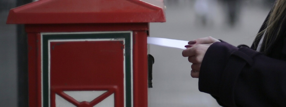 a ladies hands posting a letter into a red postbox