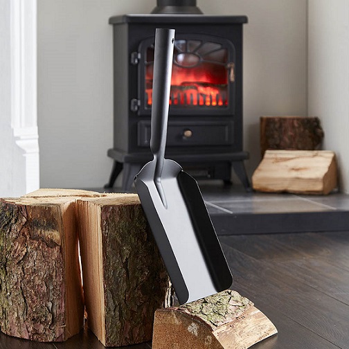 uk wholesale fireplace accessories shows a coal shovel leaning against some logs of wood in front of a fireplace.